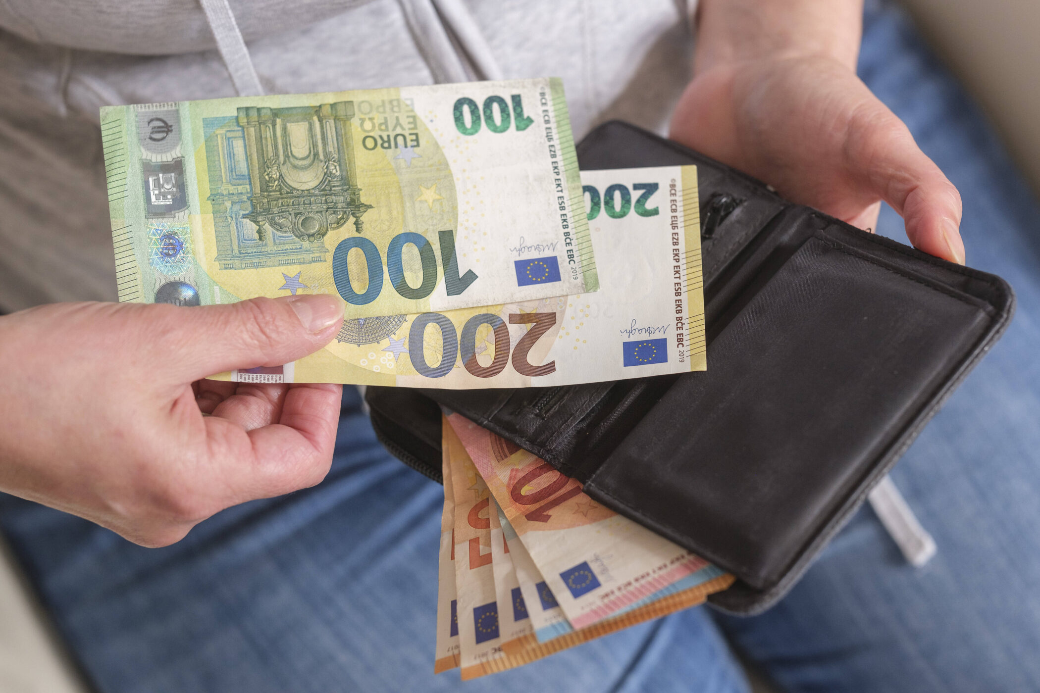 Zwei Hände halten 100- und 200-Euro-Scheine über einem schwarzen Portemonnaie.