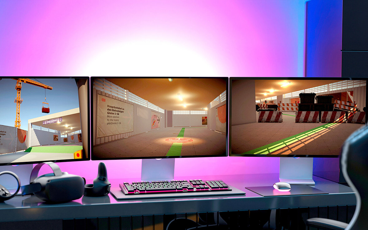 Drei Monitore mit virtueller Umgebung, VR-Headset auf Schreibtisch.