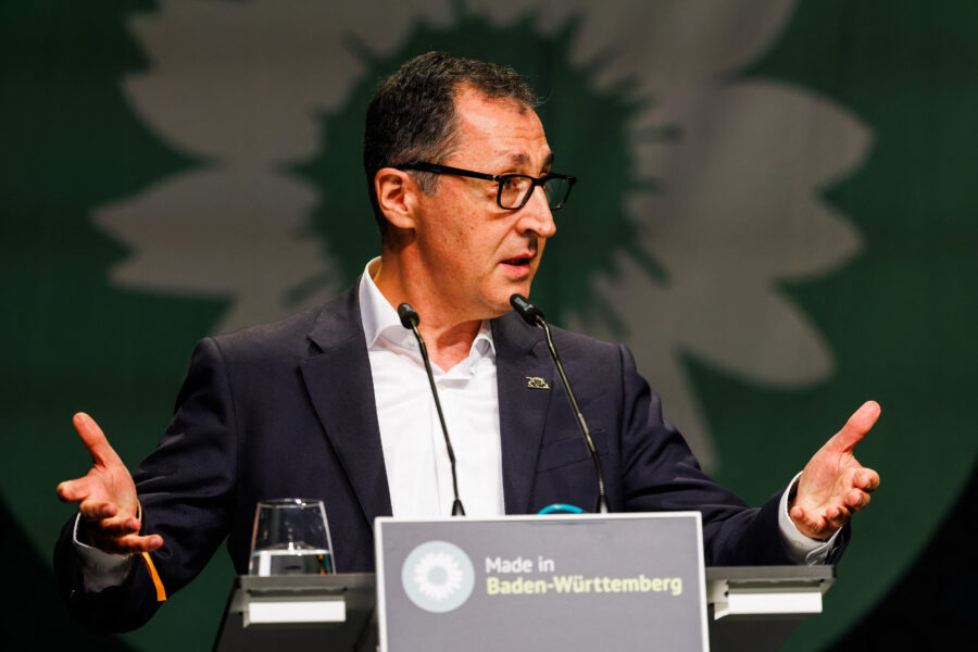 Mann am Rednerpult, spricht gestikulierend, Hintergrund mit Logo.