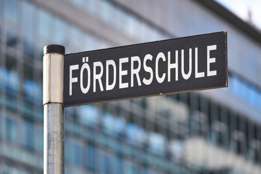 Schild mit der Aufschrift „FÖRDERSCHULE“ vor einem verschwommenen Gebäude.