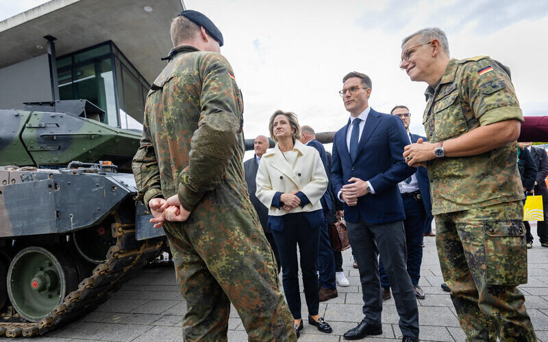 Eine Gruppe Menschen steht neben einem Militärfahrzeug auf einer Straße.