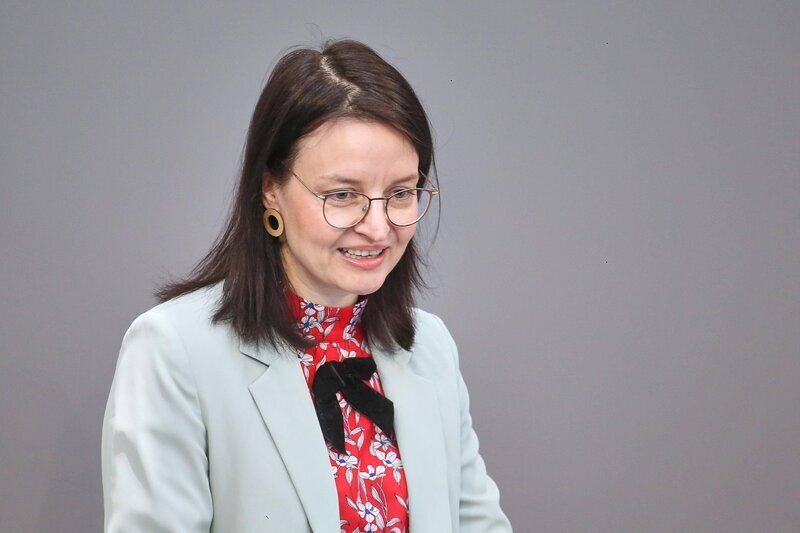 Eine Frau mit Brille und Blazer vor neutralem Hintergrund.