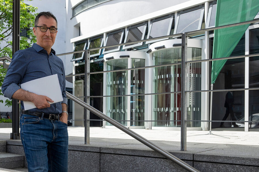 Mann hält Laptop vor modernem Gebäude mit Glasdrehtüren.
