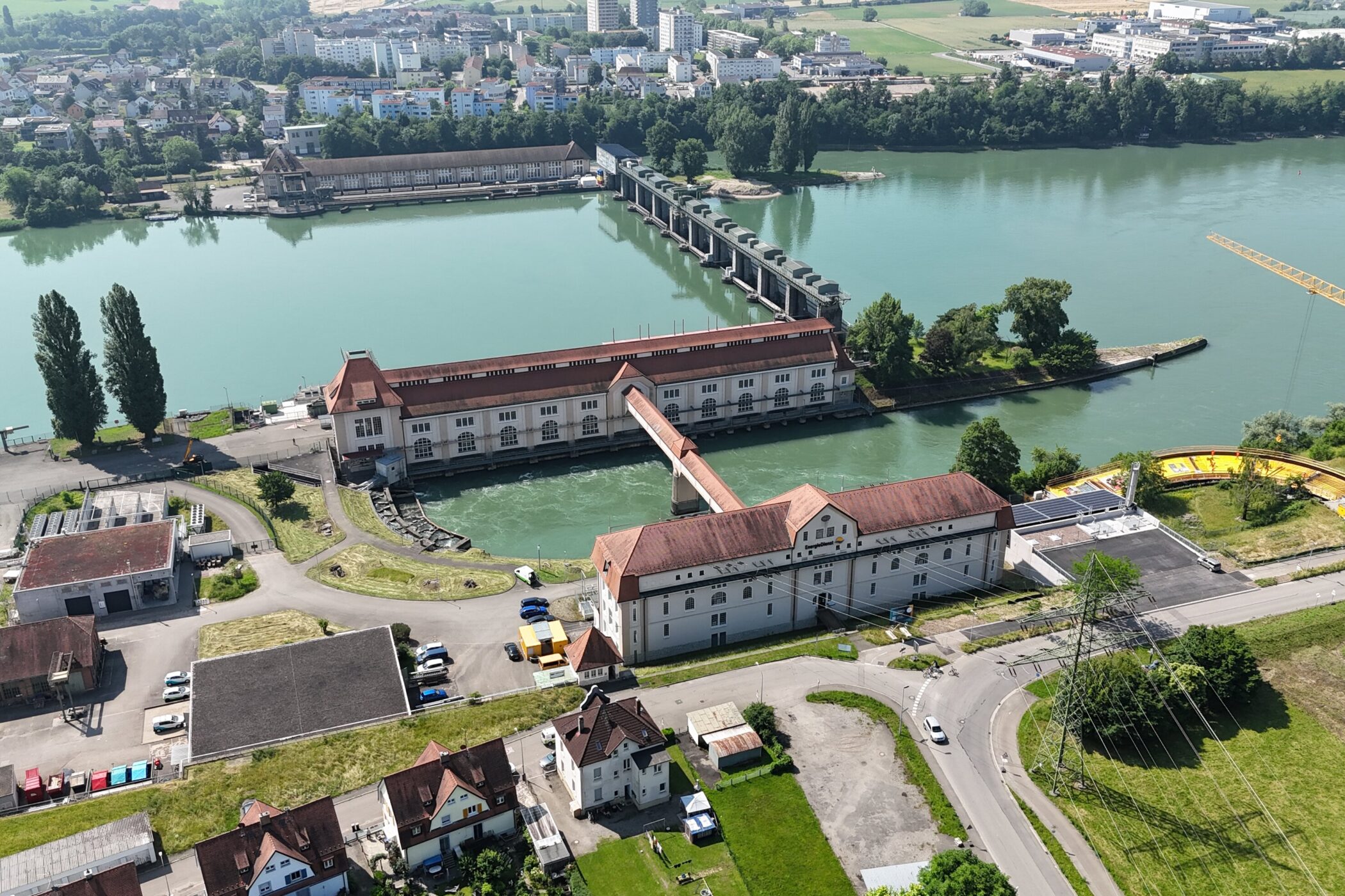 Luftaufnahme von einem Fluss, Gebäuden, Bäumen und einem Baukran.