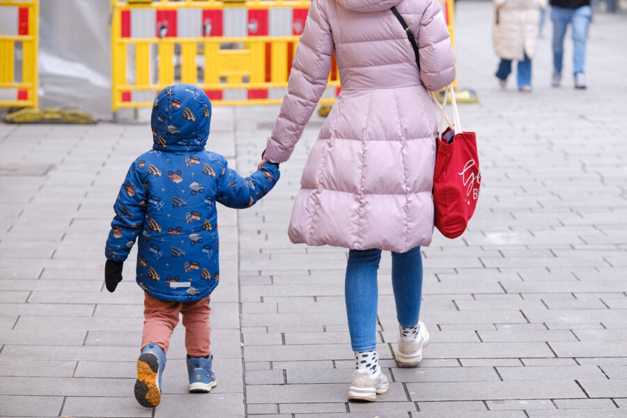 Ein Kind und eine Person gehen auf einer gepflasterten Straße.