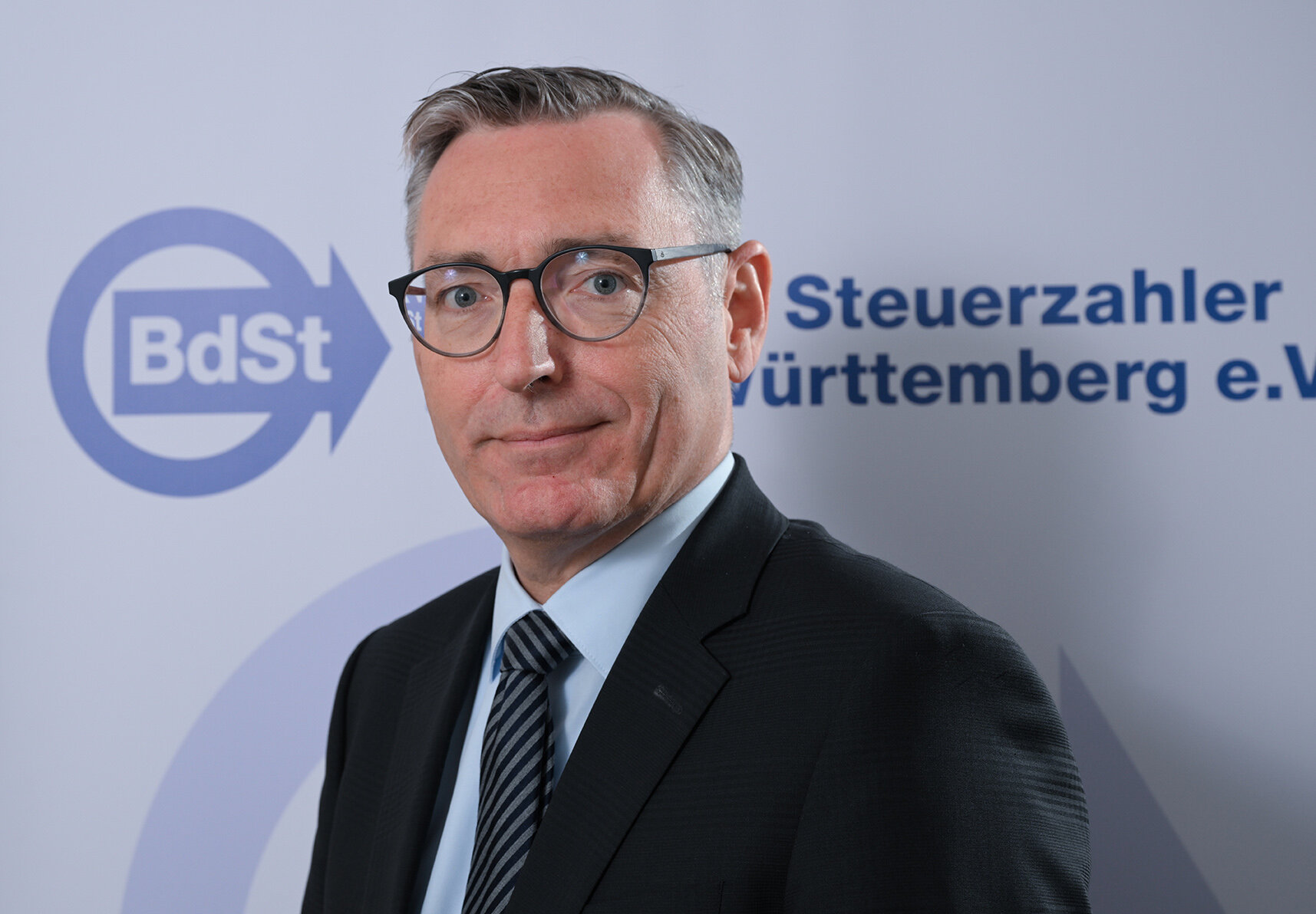 Mann mit Brille im Anzug, Hintergrund: Logo und Text BdSt Steuerzahler.