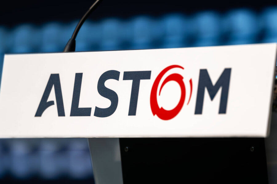 Text "ALSTOM" auf weißem Schild vor unscharfem Hintergrund.