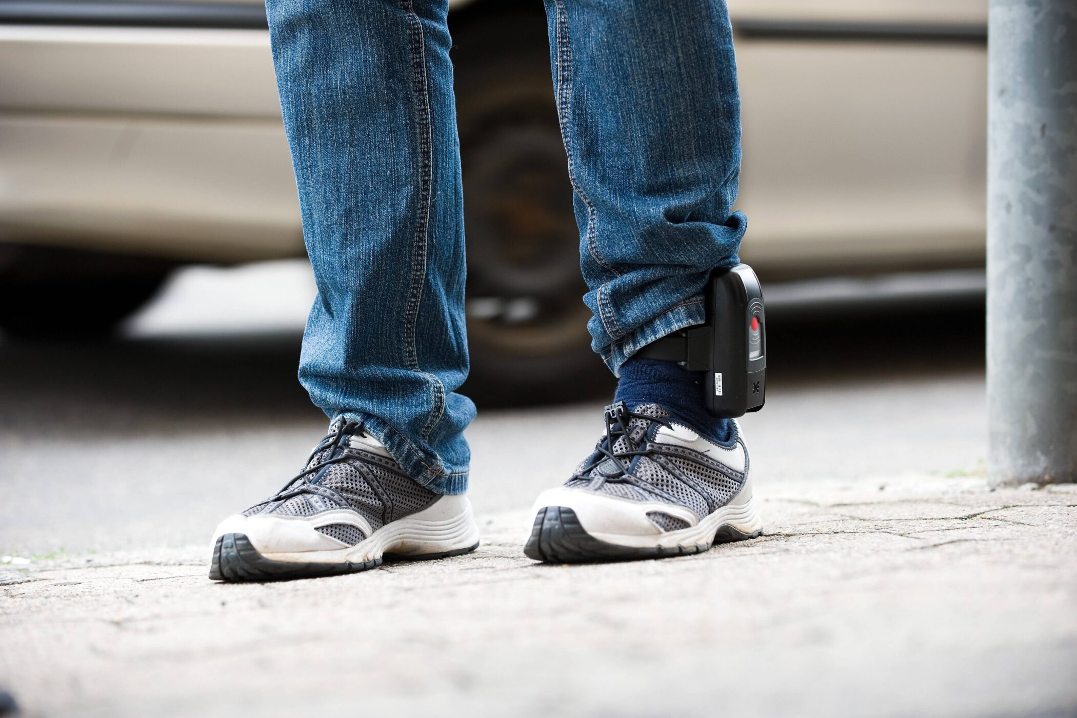 Person mit Jeans und Turnschuhen trägt ein elektronisches Fußgelenkband.