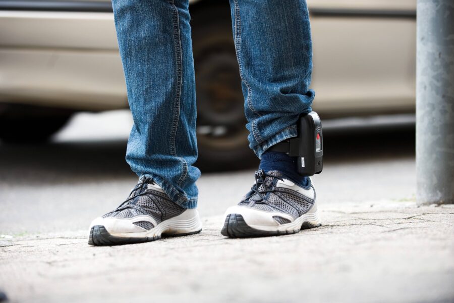 Person mit Jeans und Turnschuhen trägt ein elektronisches Fußgelenkband.
