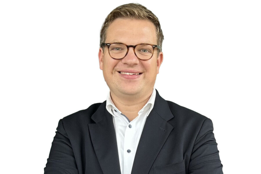 Eine Person mit Brille im Anzug vor weißem Hintergrund.