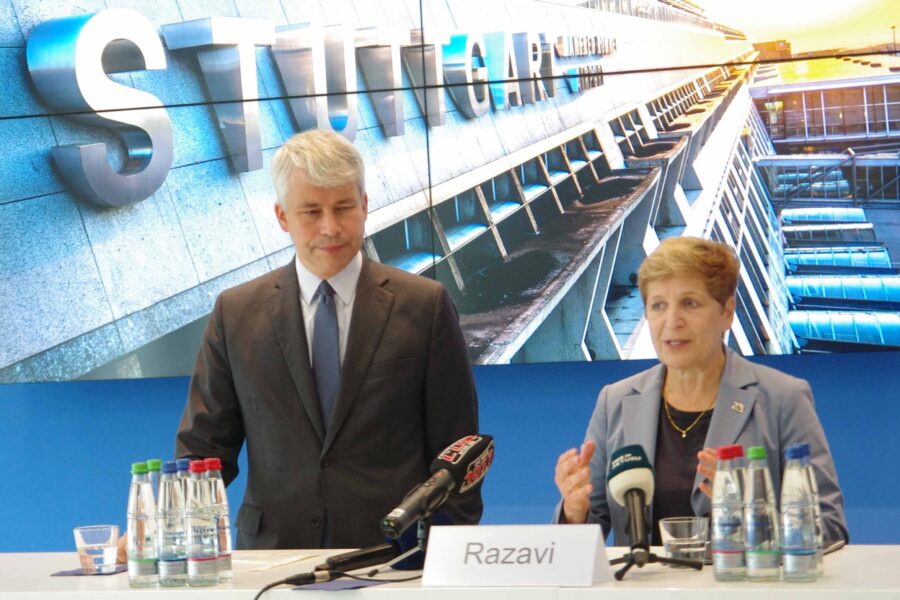 Zwei Personen stehen an einem Tisch vor dem Schriftzug "STUTTGART". Schildertext: Razavi.