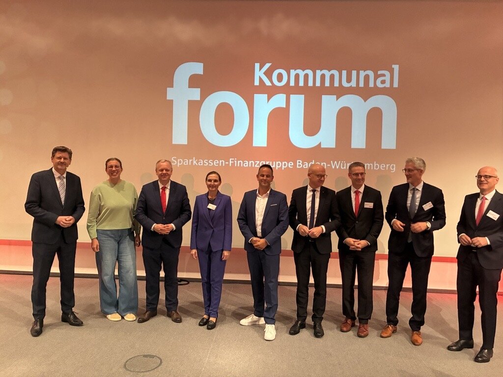 Neun Personen stehen auf einer Bühne vor der Schrift "Kommunal Forum".