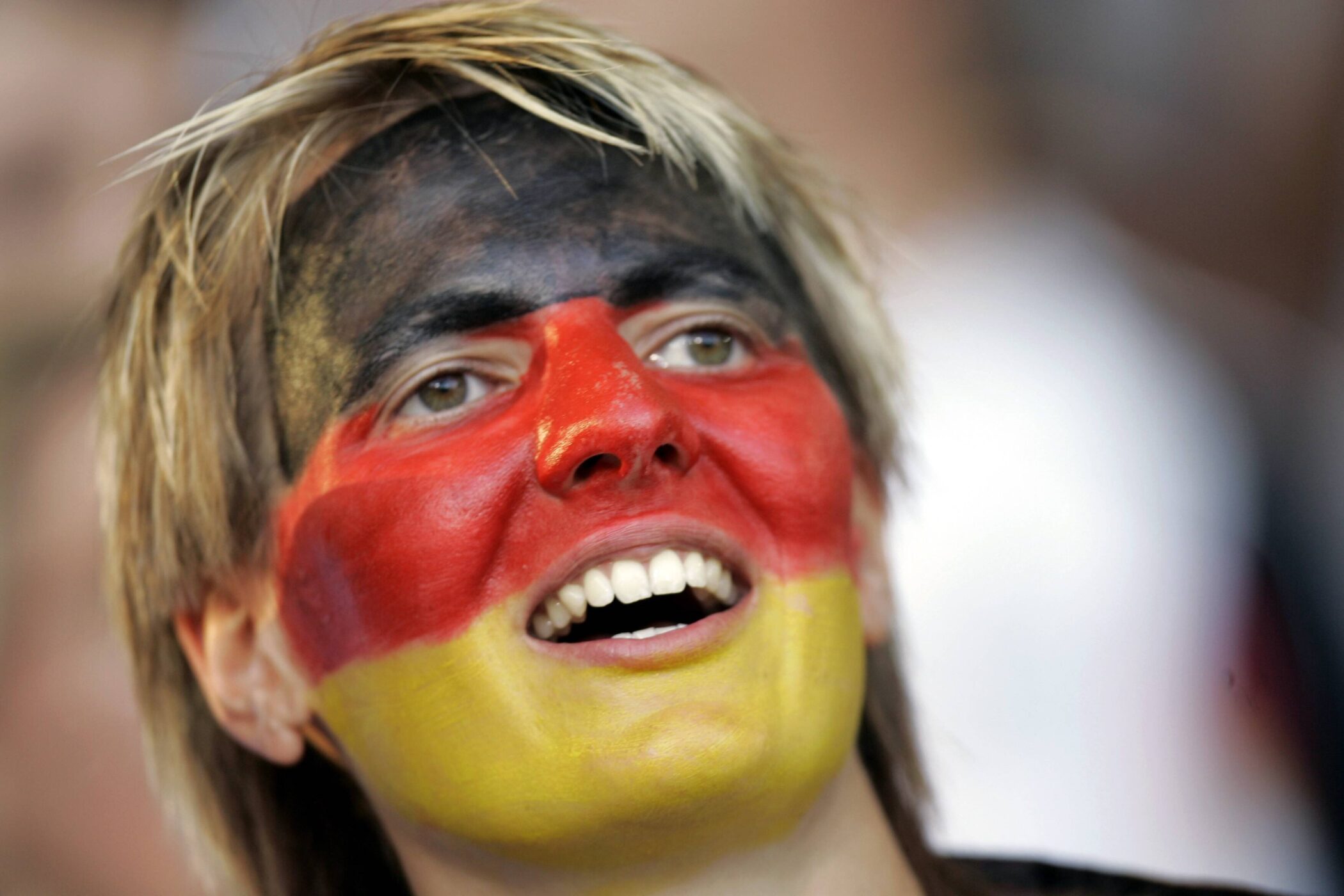 Person mit schwarz-rot-gelbem Gesicht, Mund leicht geöffnet.