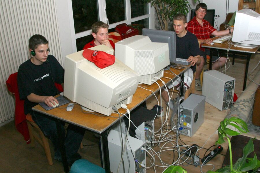 Vier Personen sitzen an Computern mit Röhrenmonitoren, Kabelgewirr auf dem Boden.