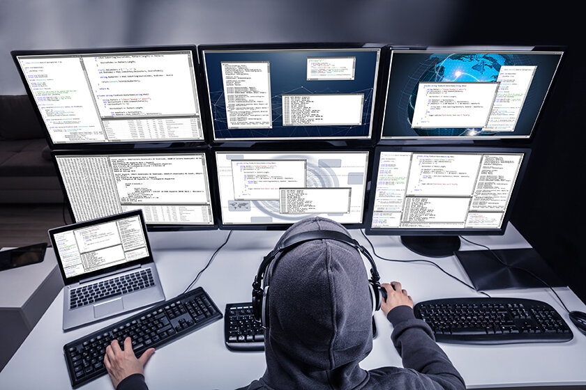 Person an Computersetup mit sechs Bildschirmen, Kopfhörer, Tastaturen und Laptop.
