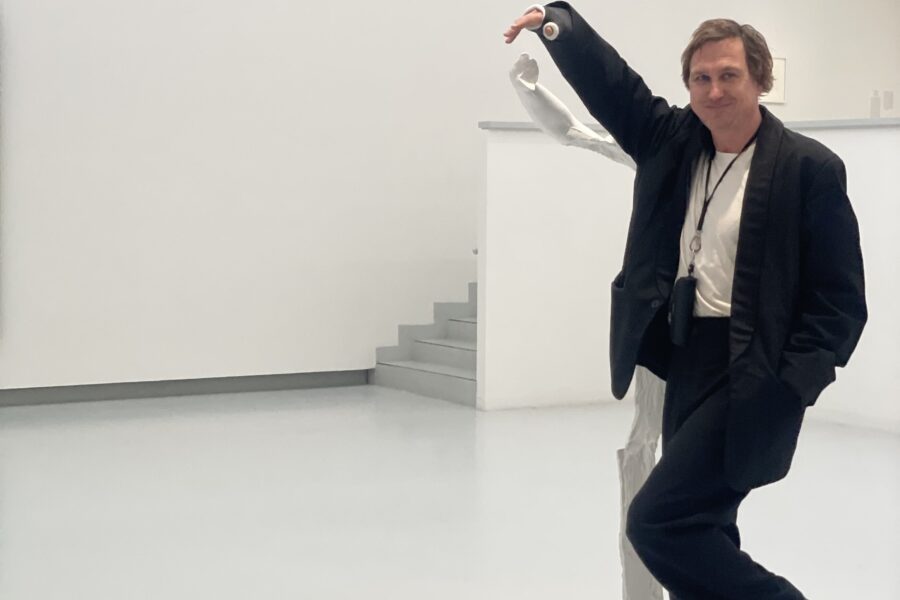 Eine Person posiert neben einer weißen Statue in einem weißen Raum.