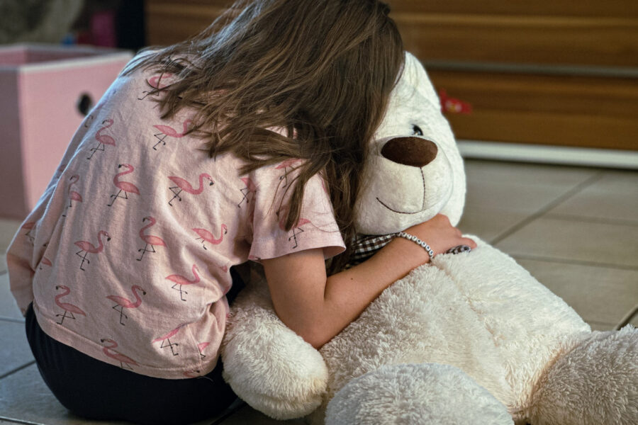 Kind umarmt großen weißen Teddybär auf dem Boden. Shirt mit Flamingos.