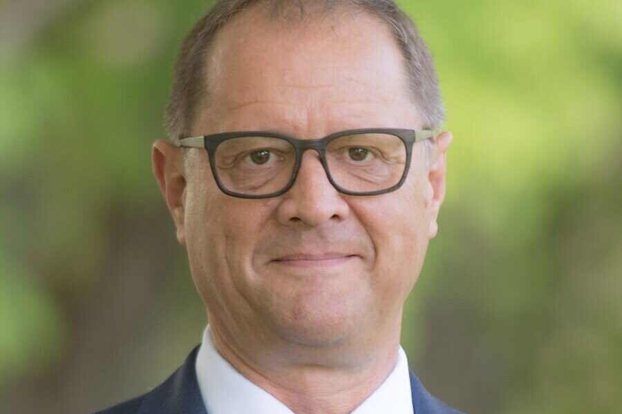 Mann mit Brille und Anzug, Hintergrund unscharf grün.