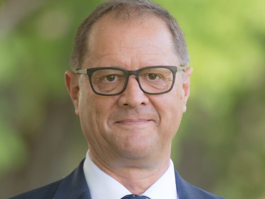 Mann mit Brille und Anzug, Hintergrund unscharf grün.