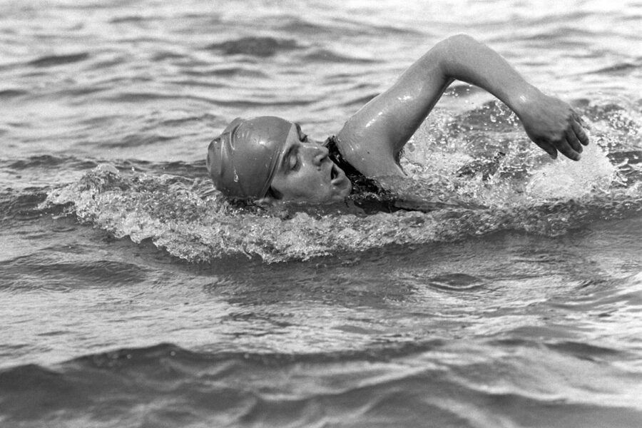 Person schwimmt im Wasser mit Badekappe, Arm zum Schwimmzug erhoben. Schwarz-Weiß-Foto.