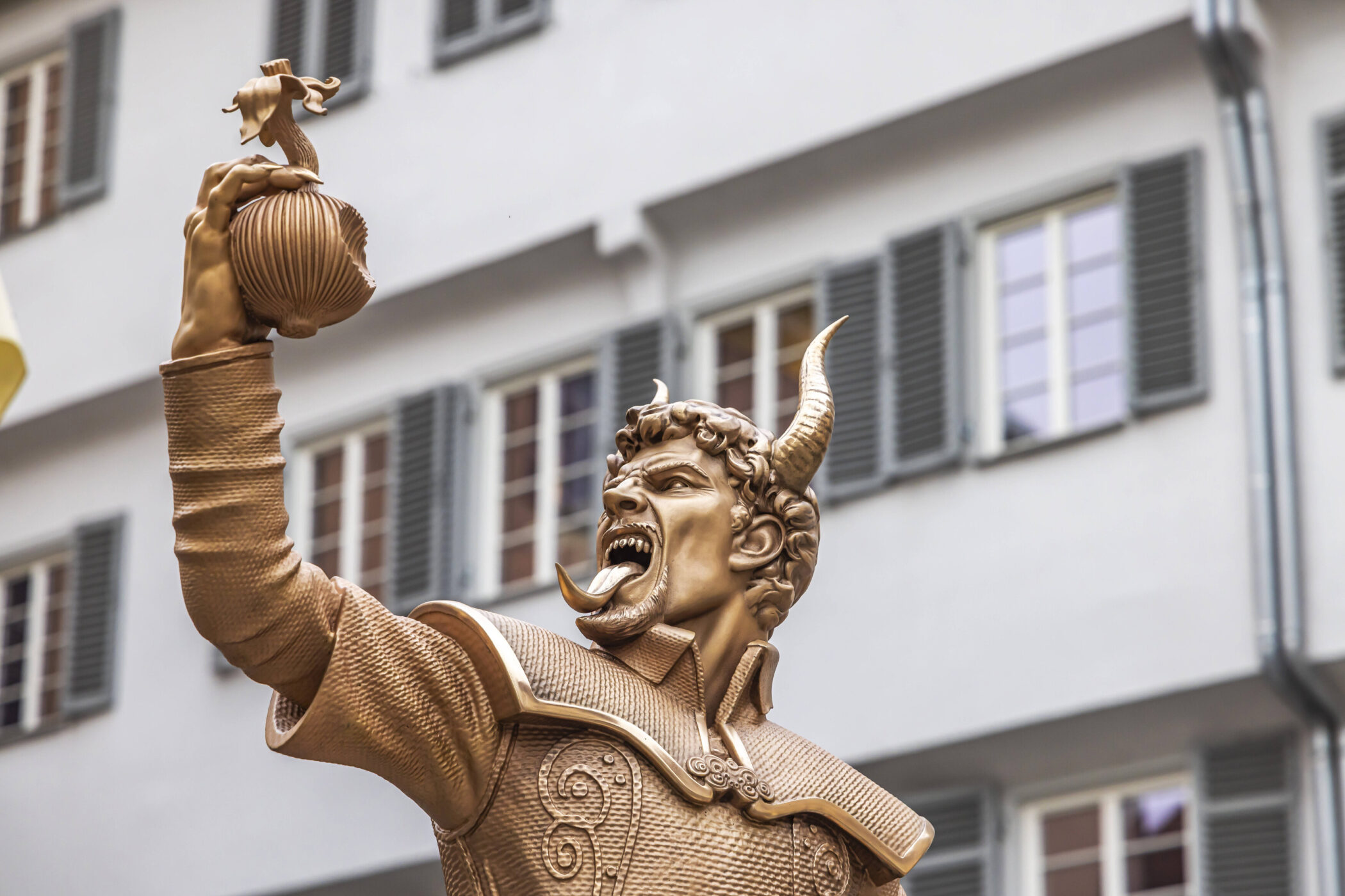 Bronzestatue eines Mannes mit Hörnern, hält einen Apfel hoch, Hintergrund Fenstergitter.