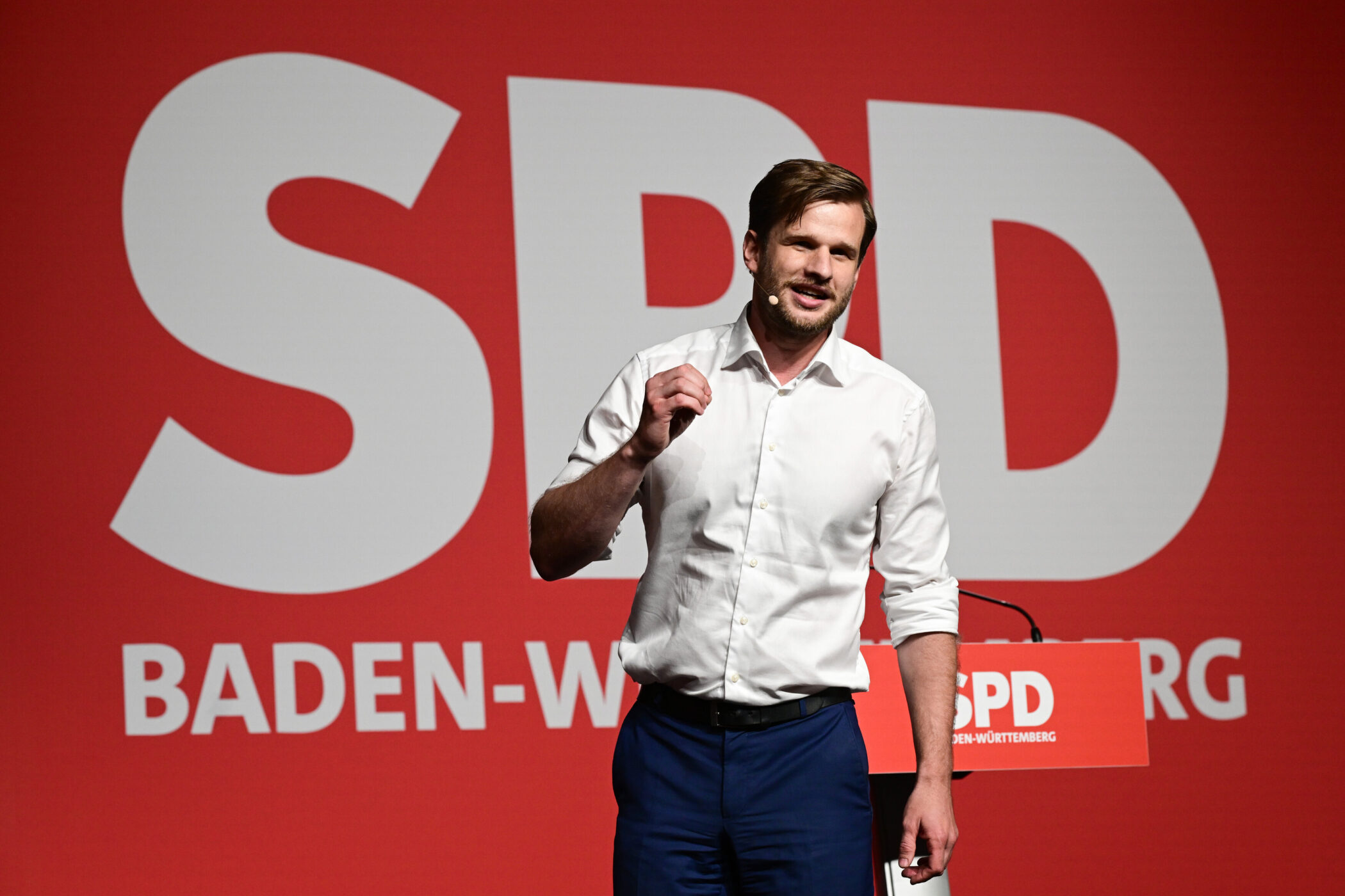 Mann im weißen Hemd spricht vor rotem Hintergrund mit „SPD BADEN-WÜRTTEMBERG“.