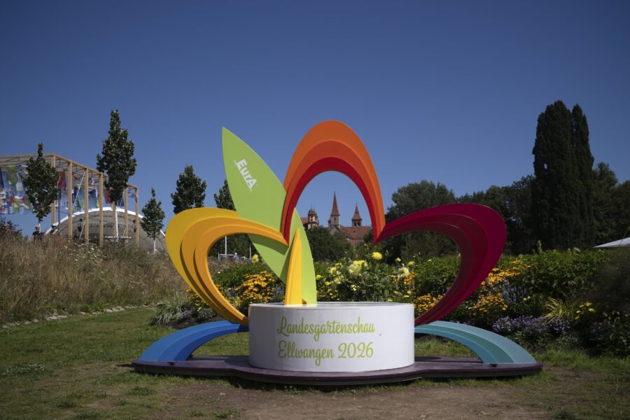 Buntes Blumenskulptur mit Text: "Landesgartenschau Ellwangen 2026", blauer Himmel.