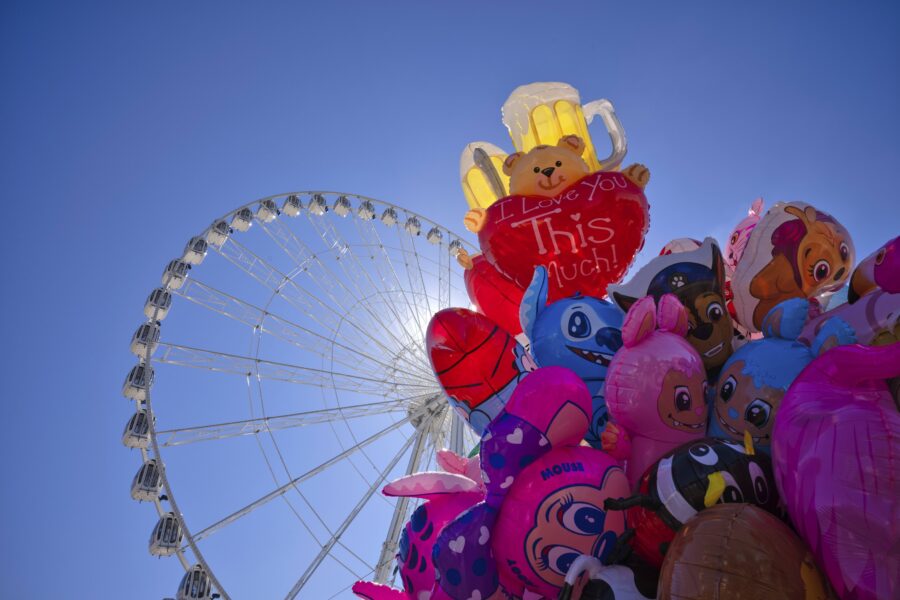 Riesenrad und bunte Luftballons vor blauem Himmel, u.a. Bär mit „I Love You“.