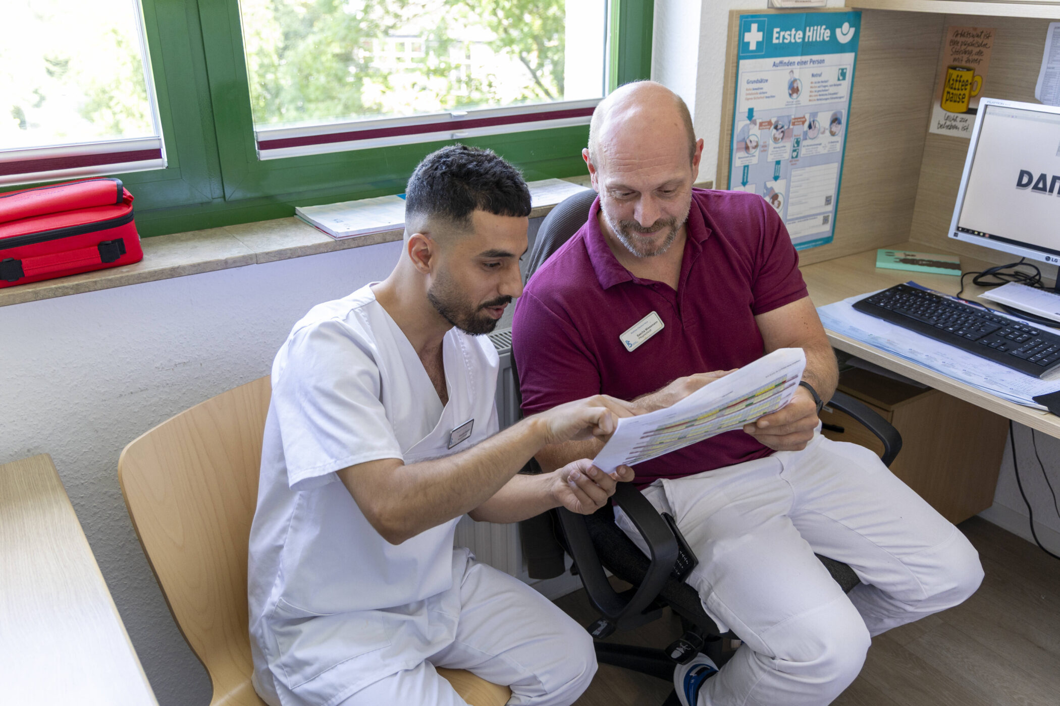Zwei Männer in medizinischer Kleidung besprechen Dokumente in einem Büro.