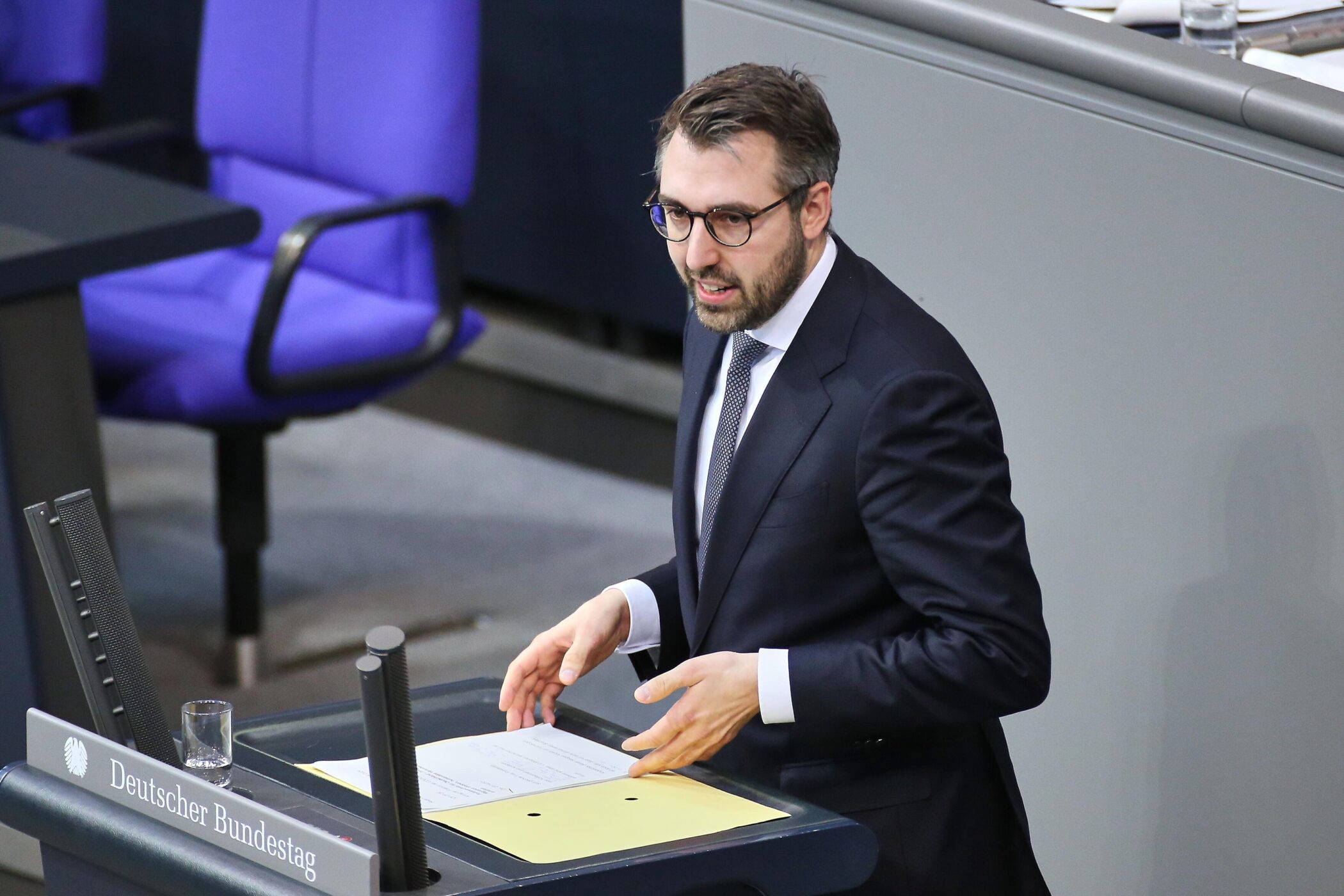 Person am Rednerpult im Bundestag, blauer Stuhl im Hintergrund.