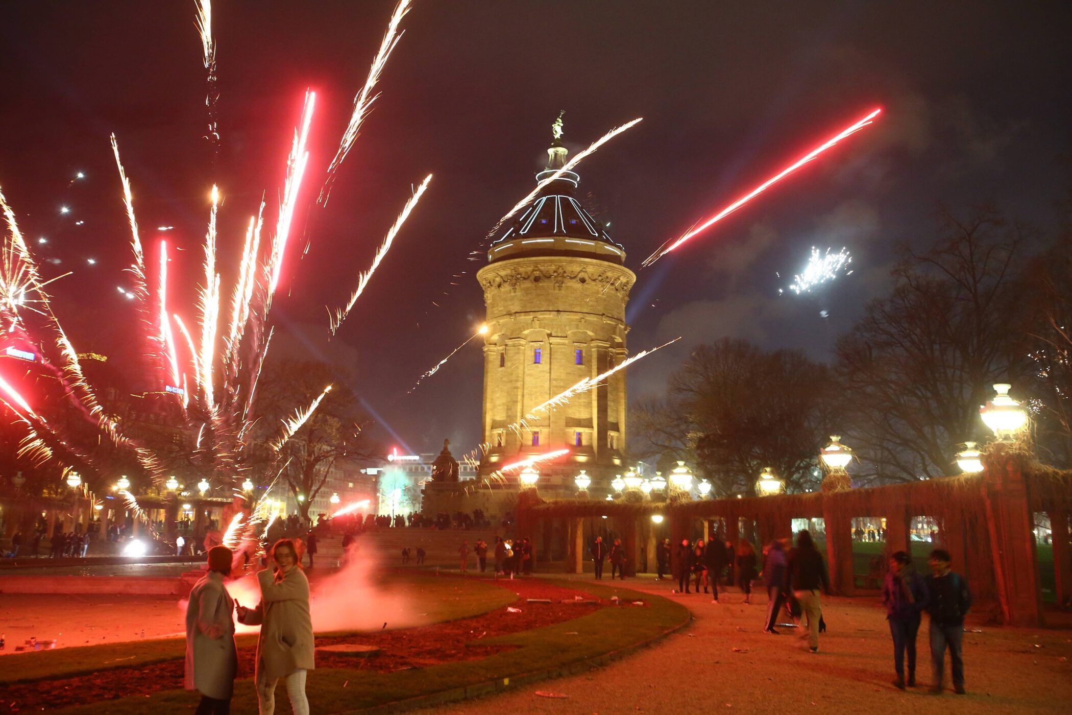 Zwei Personen im Vordergrund, Feuerwerk und beleuchteter Turm im Hintergrund.