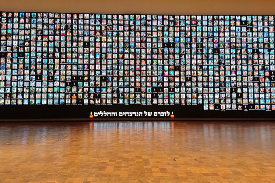 Viele Fotos von Menschen auf einer großen Leinwand, hebräischer Text darunter.