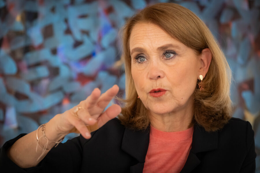 Eine Frau gestikuliert vor einem farbigen, unscharfen Hintergrund.