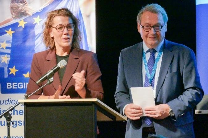 Zwei Personen an einem Podium, Hintergrund mit EU-Flagge.