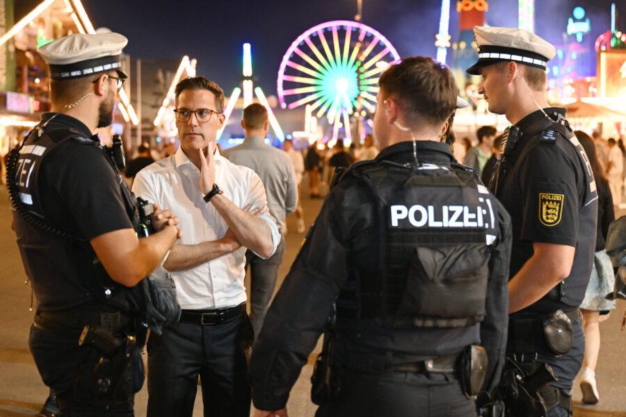 Vier Personen, darunter drei Polizisten, im Gespräch auf einem nächtlichen Festplatz.