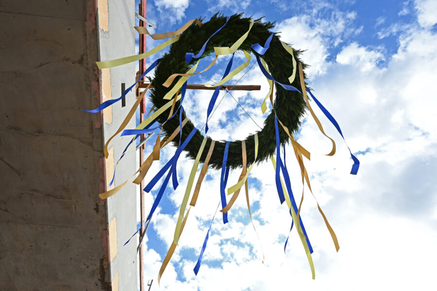 Kranz mit blauen und gelben Bändern hängt an einem Gebäude vor blauem Himmel.