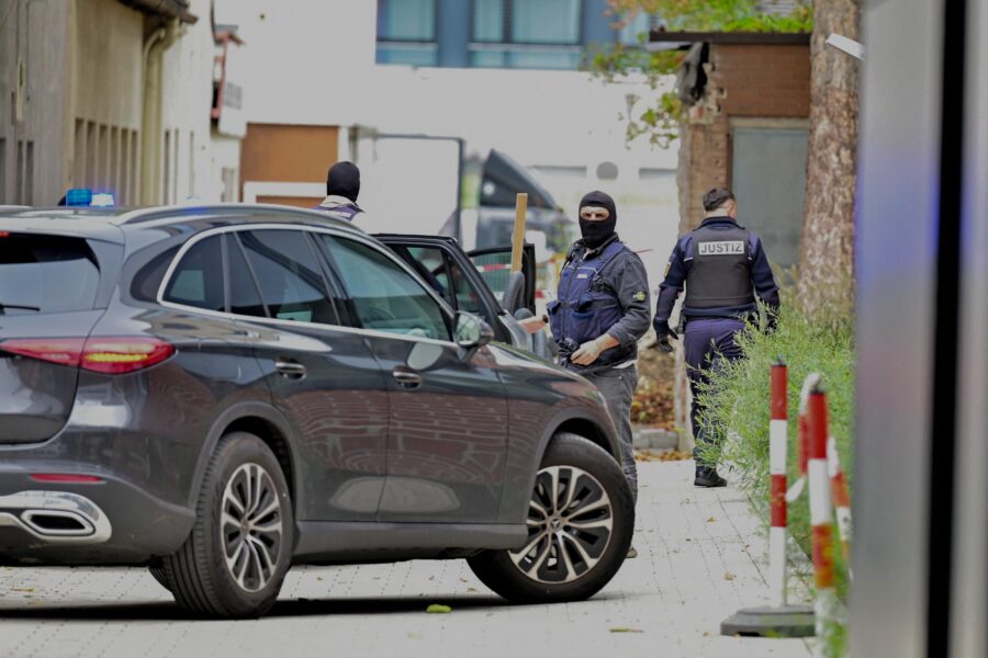 Drei Personen mit Uniform, neben einem grauen Auto, Text "Justiz" erkennbar.