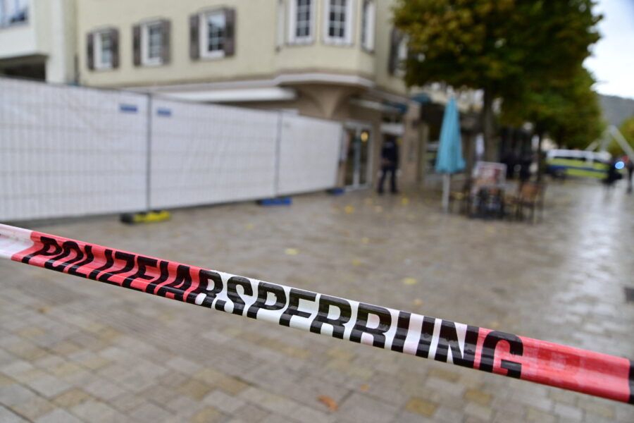 Rotes Absperrband mit „POLIZEIABSPERRUNG“ vor Geschäft und Bäumen.