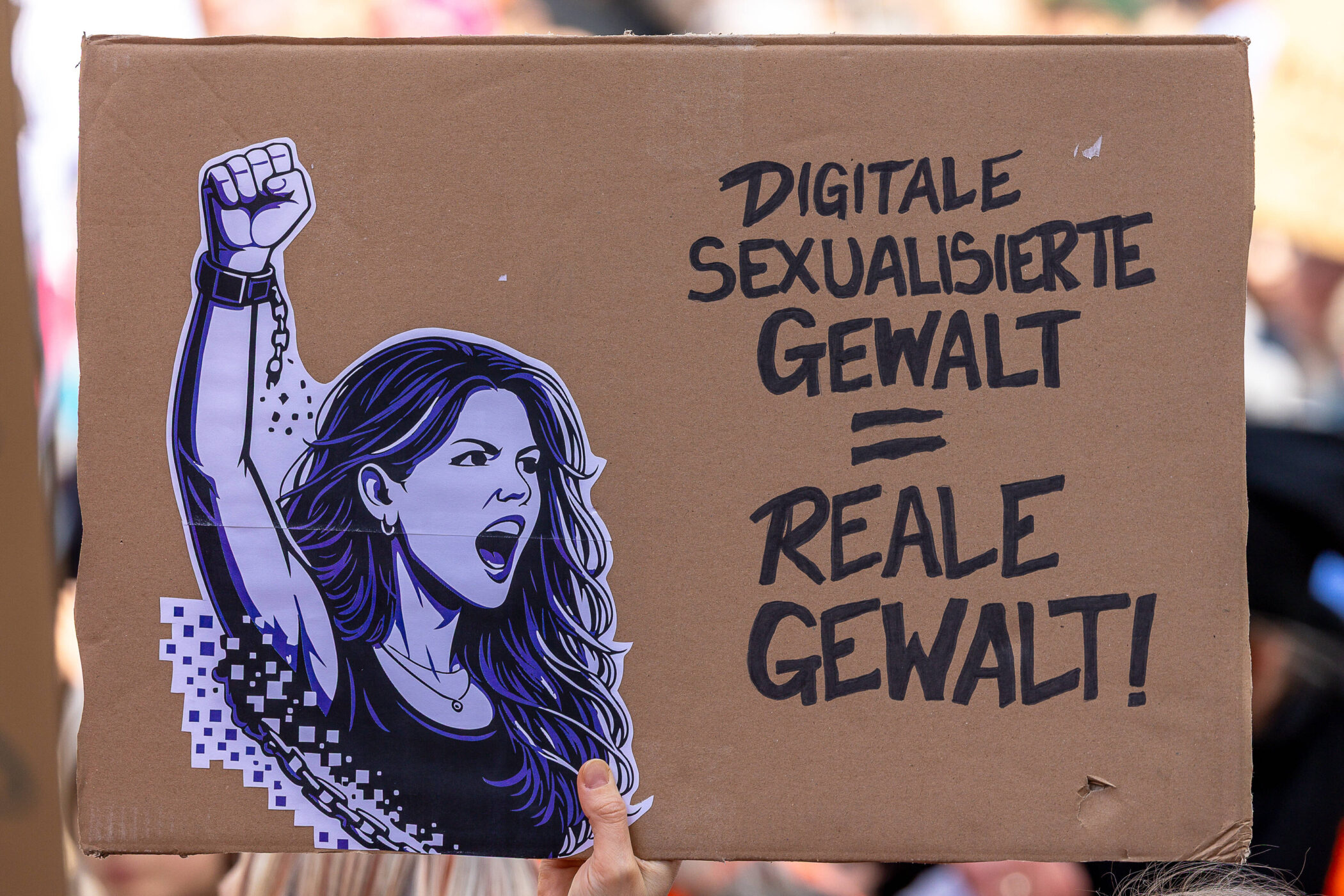 Pappschild mit Zeichnung einer Frau und Text: "Digitale sexualisierte Gewalt = reale Gewalt!"