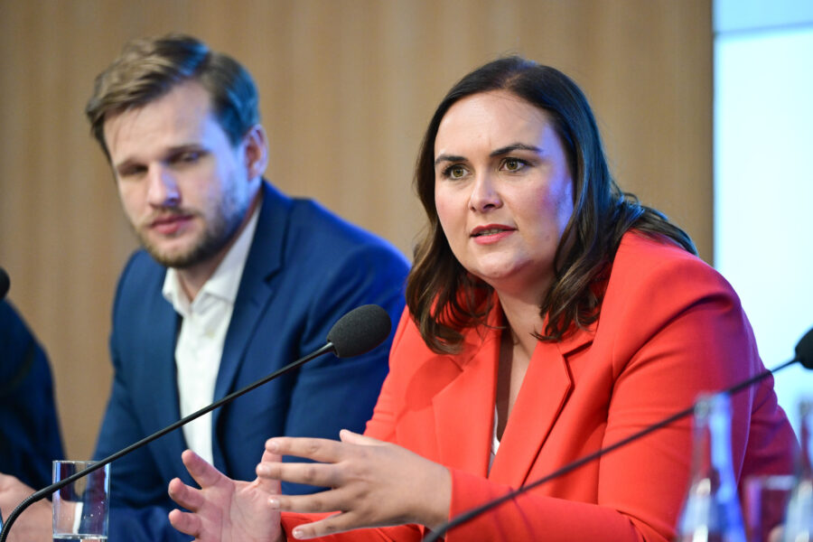 Zwei Personen bei einer Diskussion, Mikrofone vor ihnen. Eine Person spricht.