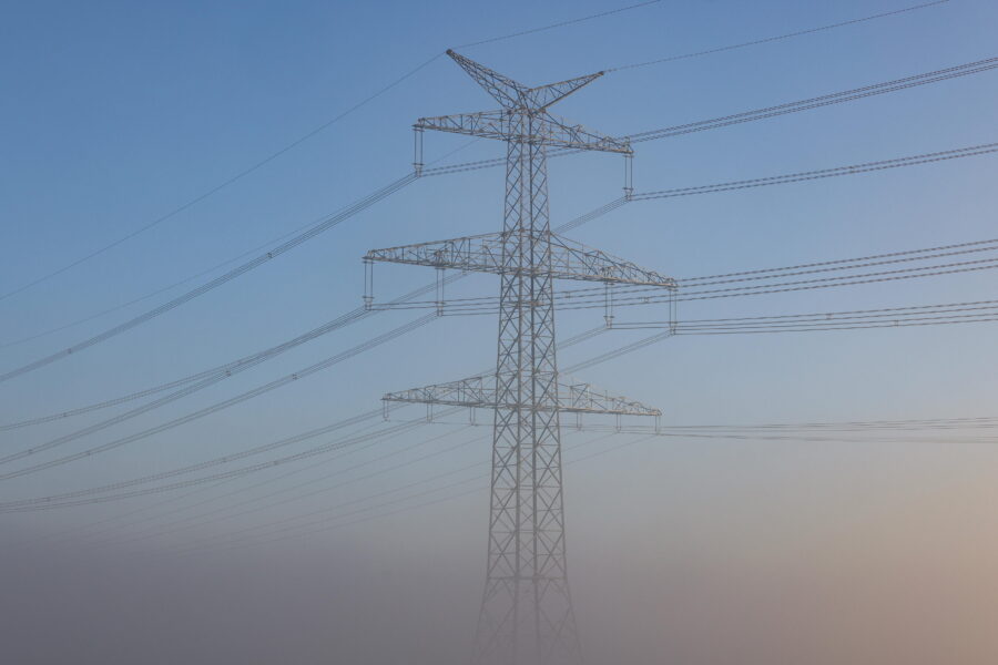 Strommast mit Hochspannungsleitungen im Nebel vor blauem Himmel.