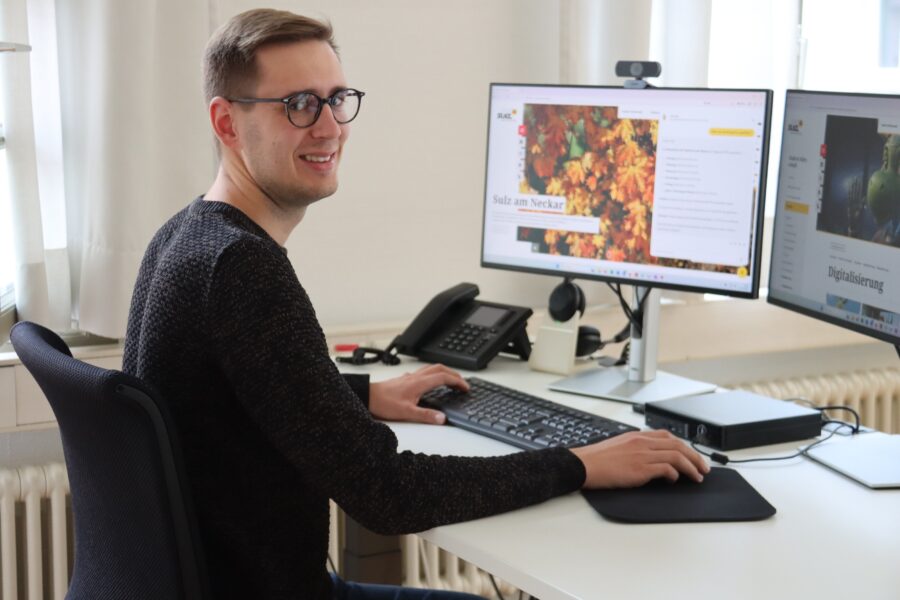 Person am Schreibtisch, arbeitet an zwei Bildschirmen, Text auf Bildschirm: Sulz am Neckar.