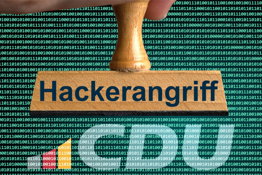 Holzstempel mit der Aufschrift „Hackerangriff“ vor Binärcode-Hintergrund.