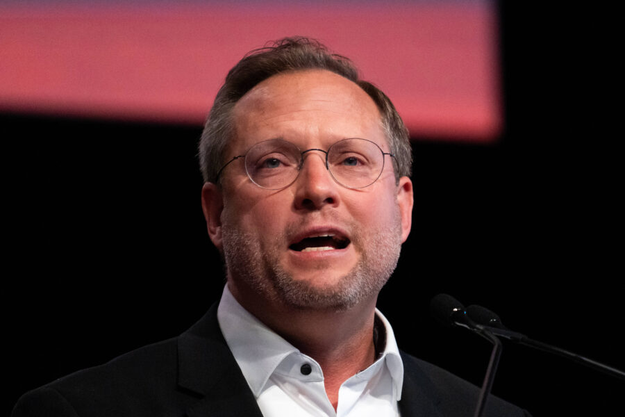 Ein Mann spricht in ein Mikrofon, mit Brille und Bart.