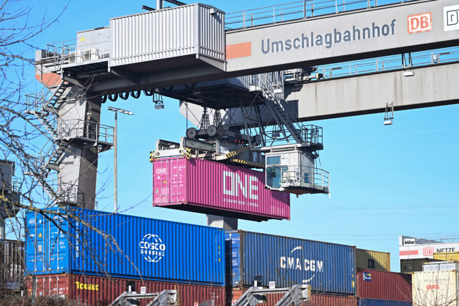 Kran im Umschlagbahnhof hebt pinken Container, andere Container darunter.