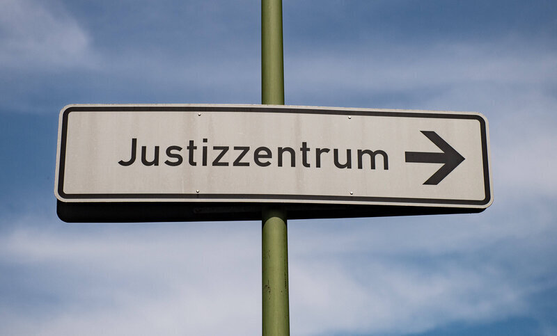 Straßenschild mit der Aufschrift „Justizzentrum“ und Pfeil nach rechts.