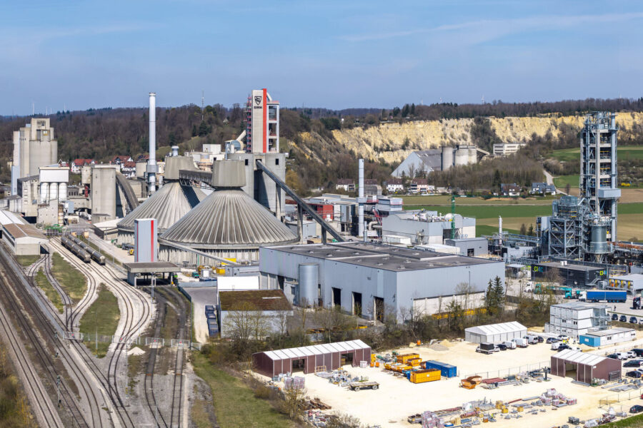 Industrieanlage mit Fabrikgebäuden, Gleisen und Lagerbereich im Vordergrund.